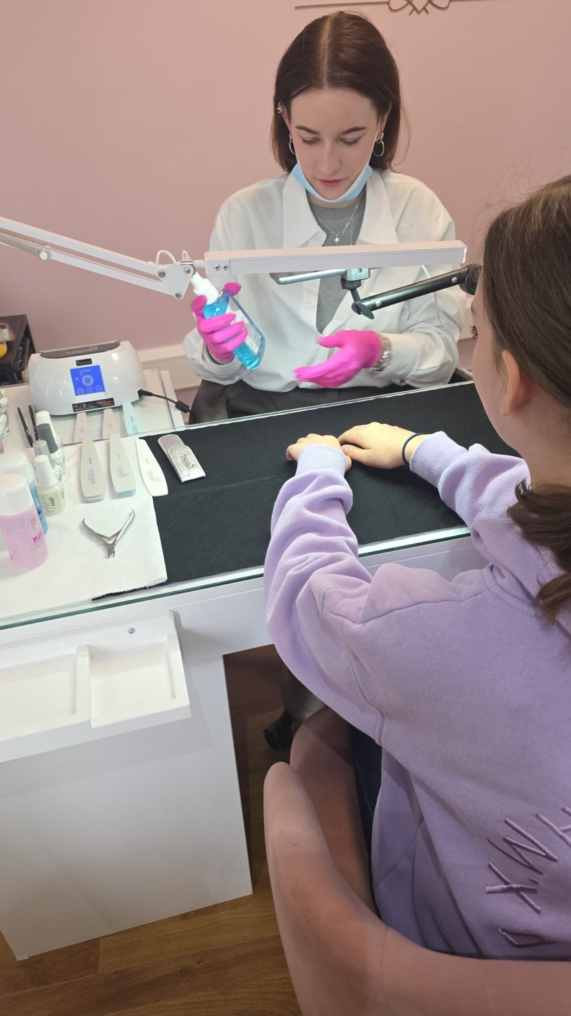 Two people practising nail application at a training table